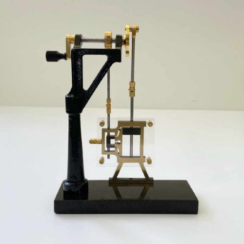fig 1. A mechanical steam engine cross-section demonstration model made of polished brass and black cast iron on a dark rectangular base.
