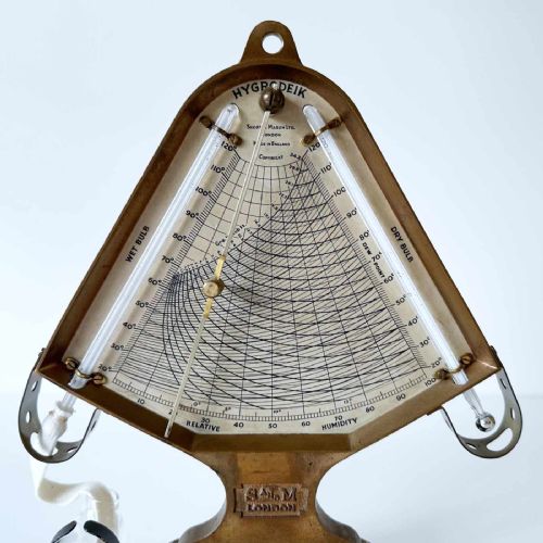 fig 1. A triangular brass Hygrodeik scientific hygrometer with glass tube thermometers on both sides and a central calculating chart with a pointer.