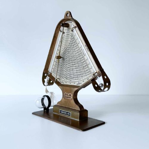 fig 2. A triangular brass Hygrodeik scientific hygrometer with glass tube thermometers on both sides and a central calculating chart with a pointer.