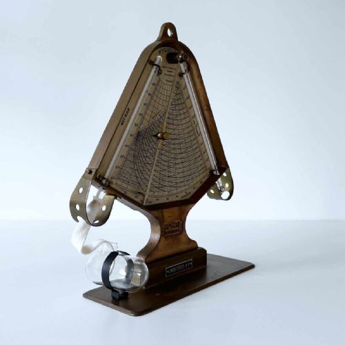 fig 4. A triangular brass Hygrodeik scientific hygrometer with glass tube thermometers on both sides and a central calculating chart with a pointer.