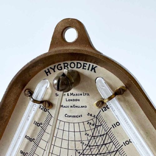 fig 5. A triangular brass Hygrodeik scientific hygrometer with glass tube thermometers on both sides and a central calculating chart with a pointer.