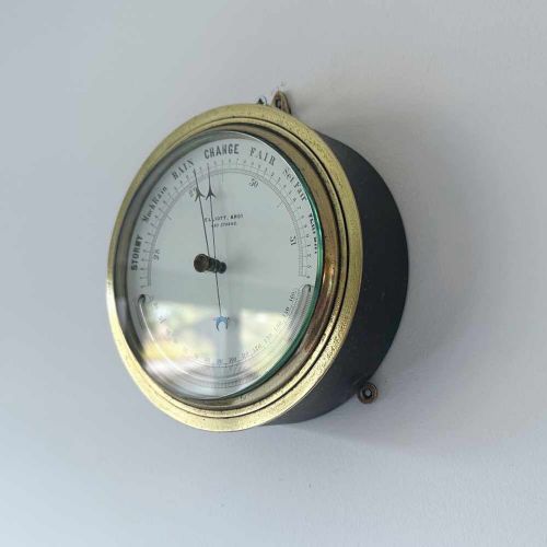 fig 2. A circular Victorian brass aneroid barometer featuring a white enamel dial with black atmospheric pressure readings and blued steel hands.