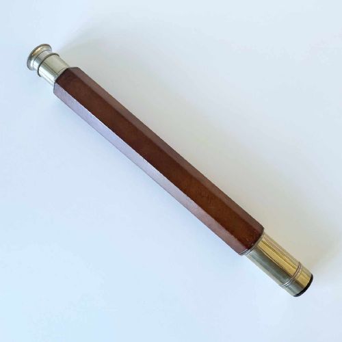 fig 3. A Victorian brass single draw marine telescope with a brown hexagonal barrel mounted on a dark wooden display stand.
