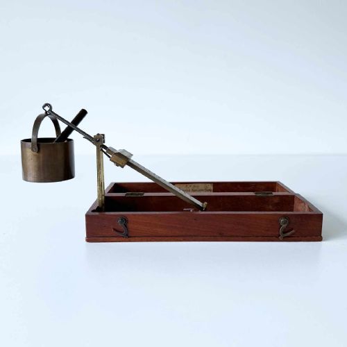 fig 1. An antique brass portable chondrometer scale featuring a small bucket suspended from a graduated beam, resting within a fitted mahogany case with printed paper labels.