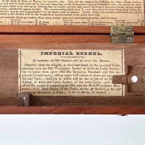 fig 4. An antique brass portable chondrometer scale featuring a small bucket suspended from a graduated beam, resting within a fitted mahogany case with printed paper labels.