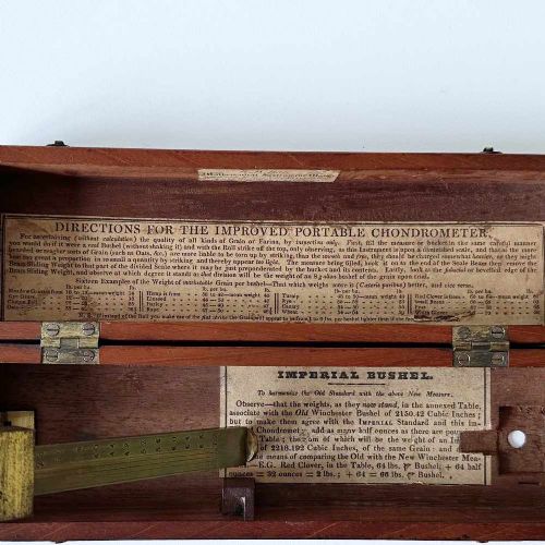 fig 5. An antique brass portable chondrometer scale featuring a small bucket suspended from a graduated beam, resting within a fitted mahogany case with printed paper labels.