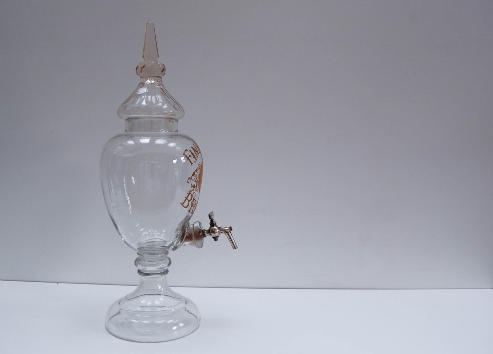 A clear glass spirit dispenser featuring gilt typography reading Fine Pale Brandy, a spire finial lid, and a brass spigot at the base. View II