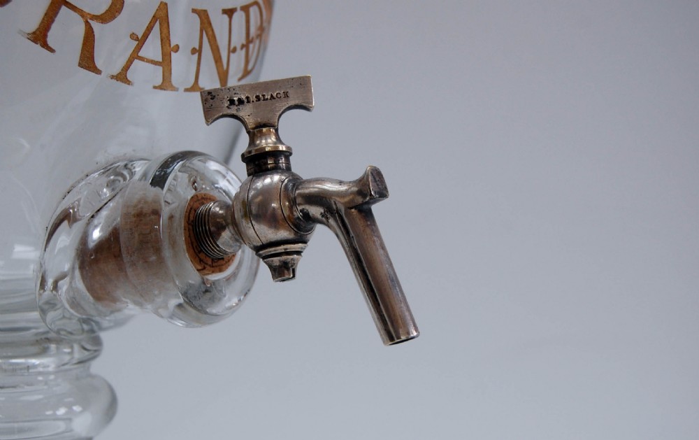 A clear glass spirit dispenser featuring gilt typography reading Fine Pale Brandy, a spire finial lid, and a brass spigot at the base. View VIII