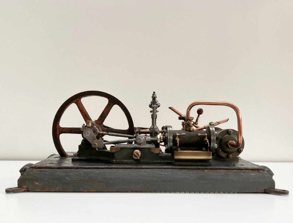 Late nineteenth-century stationary steam engine scale model with a large flywheel, brass valves, and copper piping mounted on a painted rectangular plinth.