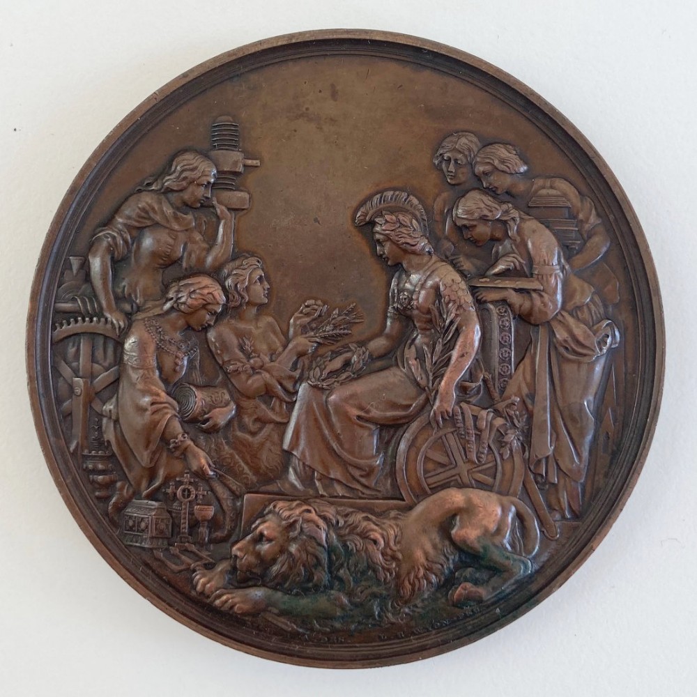 A circular Victorian bronze prize medal featuring classical figures representing arts and industry surrounding Britannia above a reclining lion.