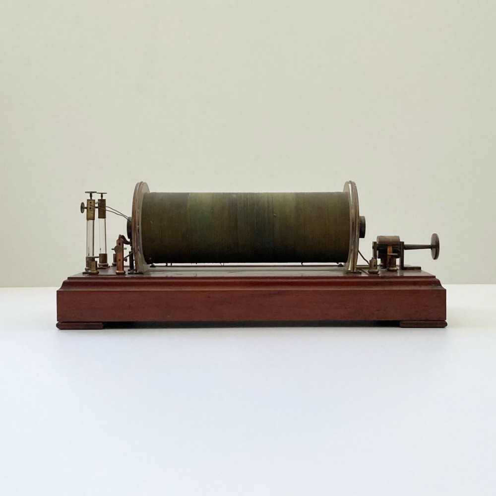 An antique 19th-century Ruhmkorff induction coil featuring a central cloth-wrapped wire cylinder, brass fittings, glass discharge tubes, and a polished mahogany base.