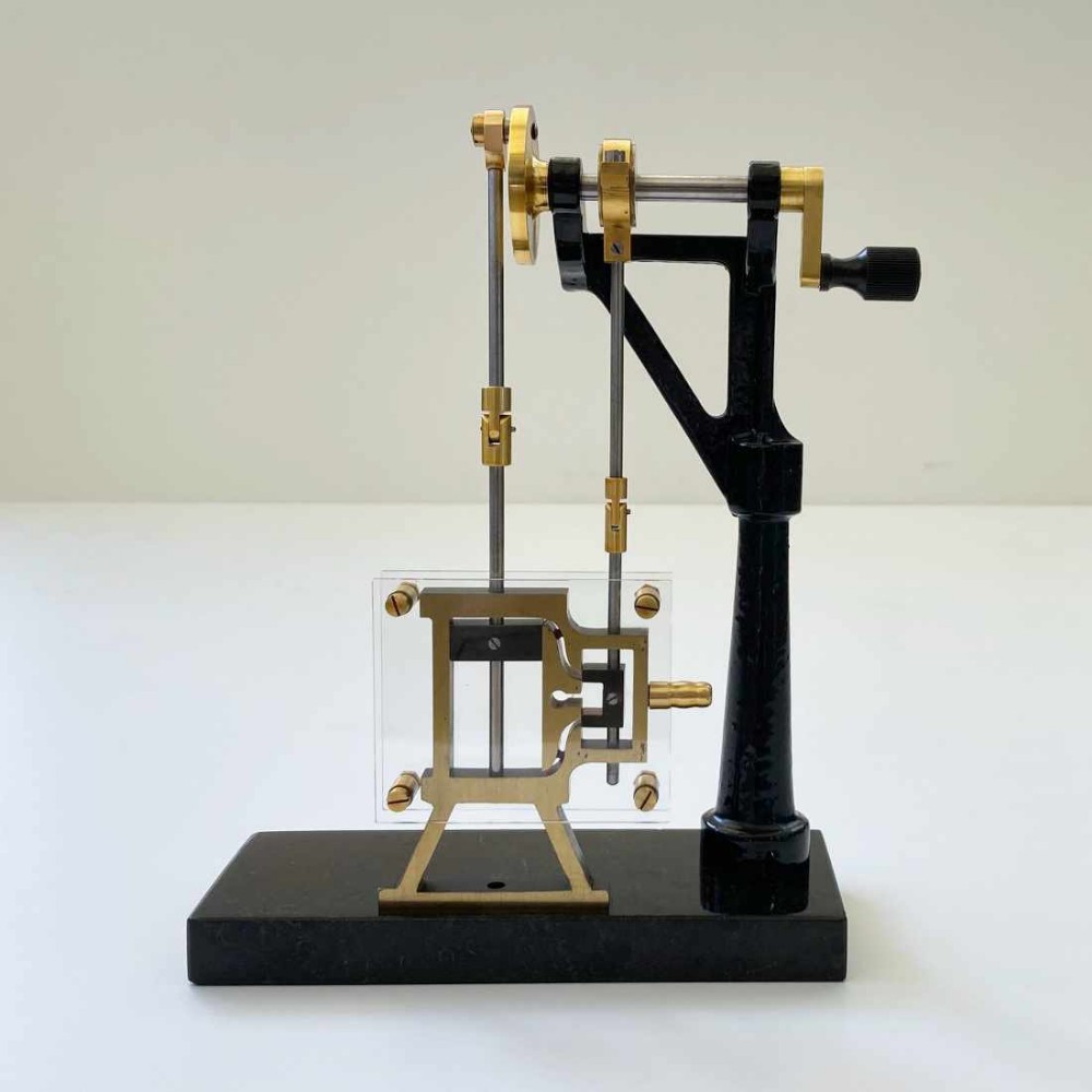 A mechanical steam engine cross-section demonstration model made of polished brass and black cast iron on a dark rectangular base.