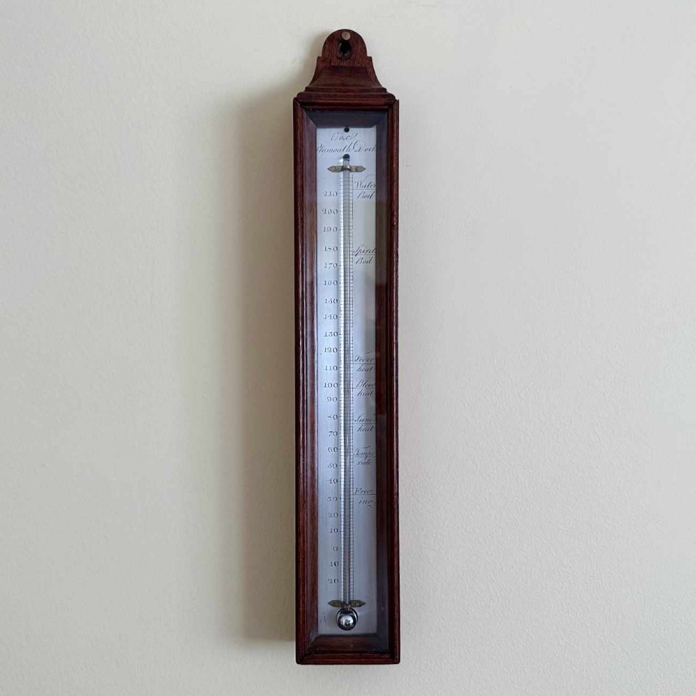 A vertical George III mahogany cased wall thermometer featuring a glazed front, silvered register scale, and top hanging loop.