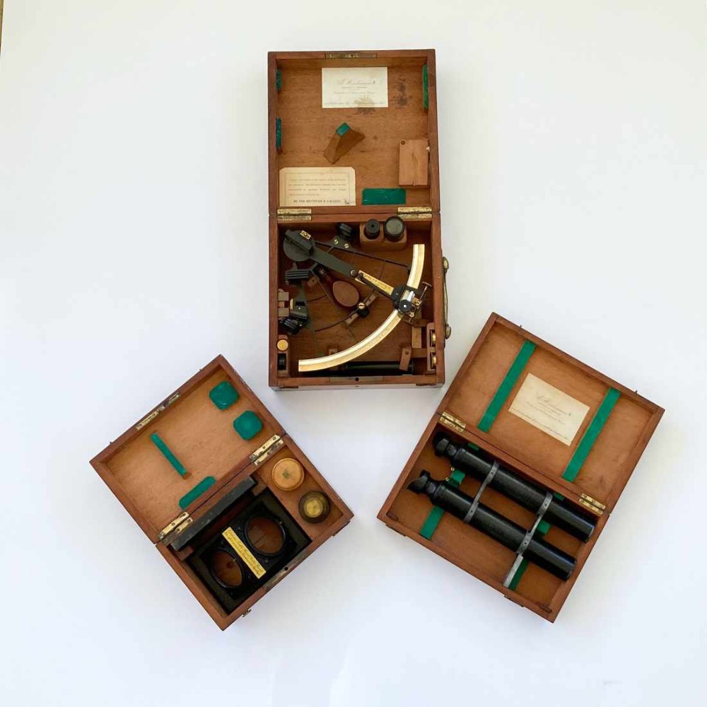 An antique French marine navigation set displayed in three open fitted mahogany cases containing a brass sextant, telescopes, and optical filters.