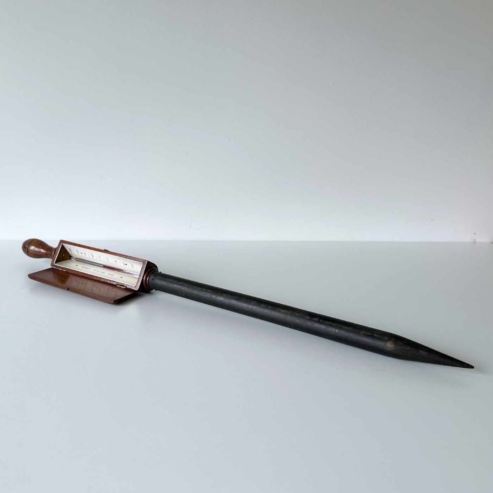 A Victorian hotbed soil thermometer featuring a long black pointed iron spike attached to a dark wooden housing with a open hinged protective lid revealing a glass scale.
