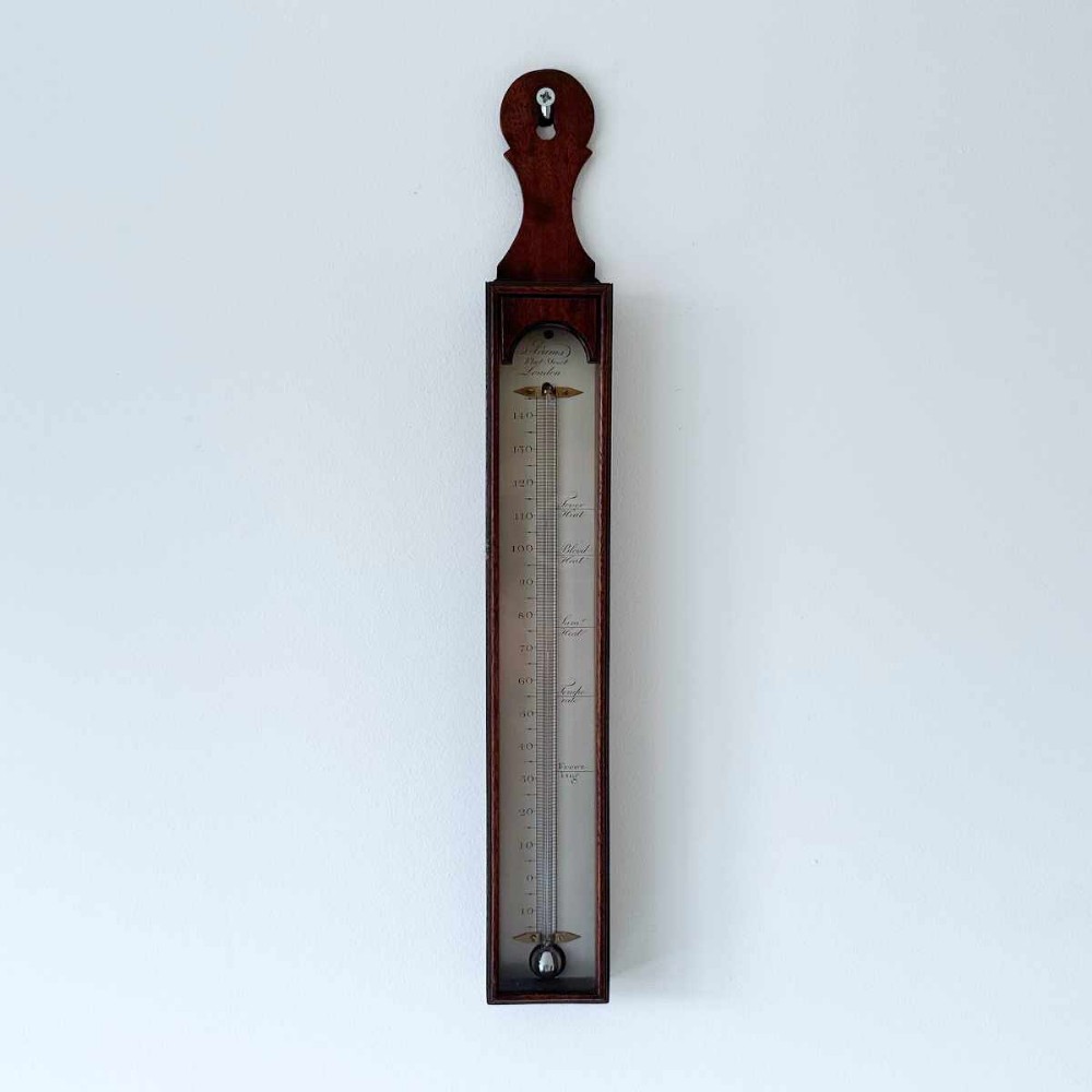 An 18th-century vertical mahogany cased wall thermometer with an engraved scale plate and glass capillary tube.