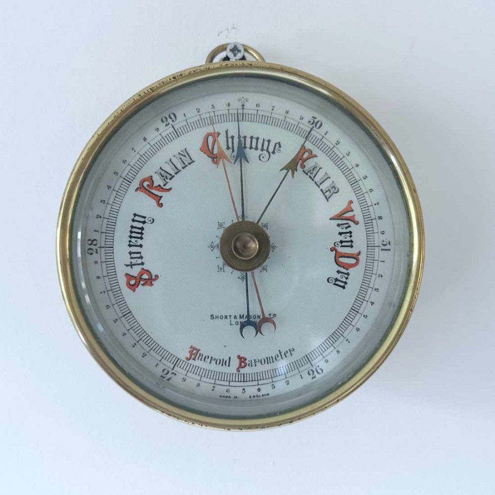 A circular brass wall-hanging aneroid barometer featuring a silvered dial with Gothic lettering, calibrated scale, and multiple indicator pointers.
