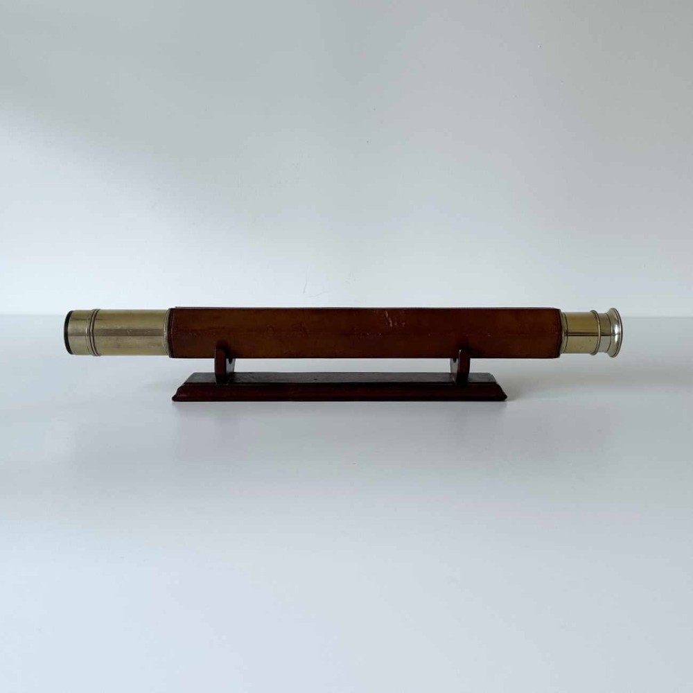 A Victorian brass single draw marine telescope with a brown hexagonal barrel mounted on a dark wooden display stand.