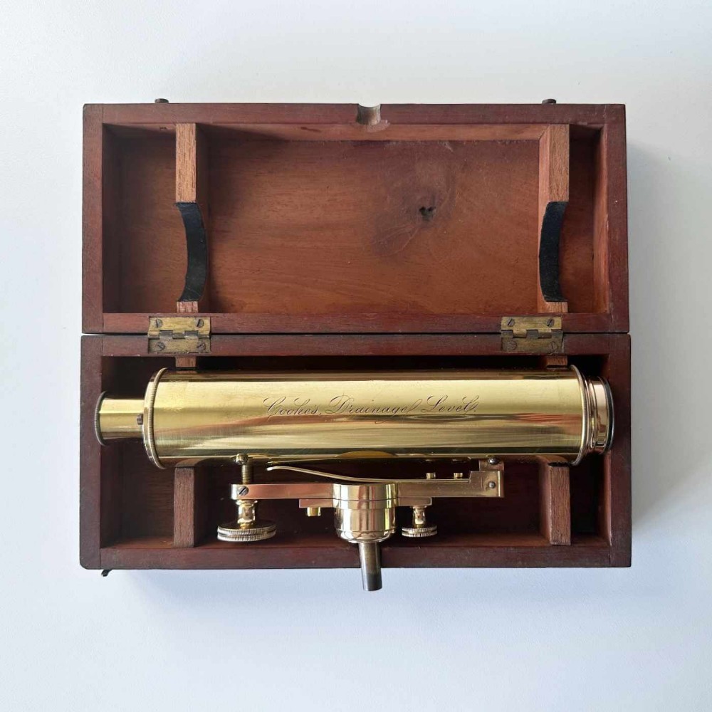 An antique brass optical surveying drainage level positioned inside a open fitted mahogany wooden box.