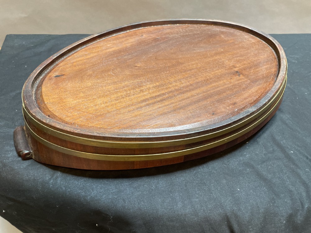 A Georgian Revival oval mahogany serving tray featuring a raised rim, integrated handles, and a brass band outer trim. View VI