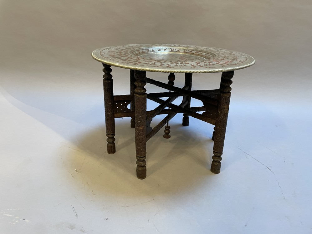 A low circular occasional table featuring an intricately etched multi-metal tray top resting on a dark carved wooden base. View V