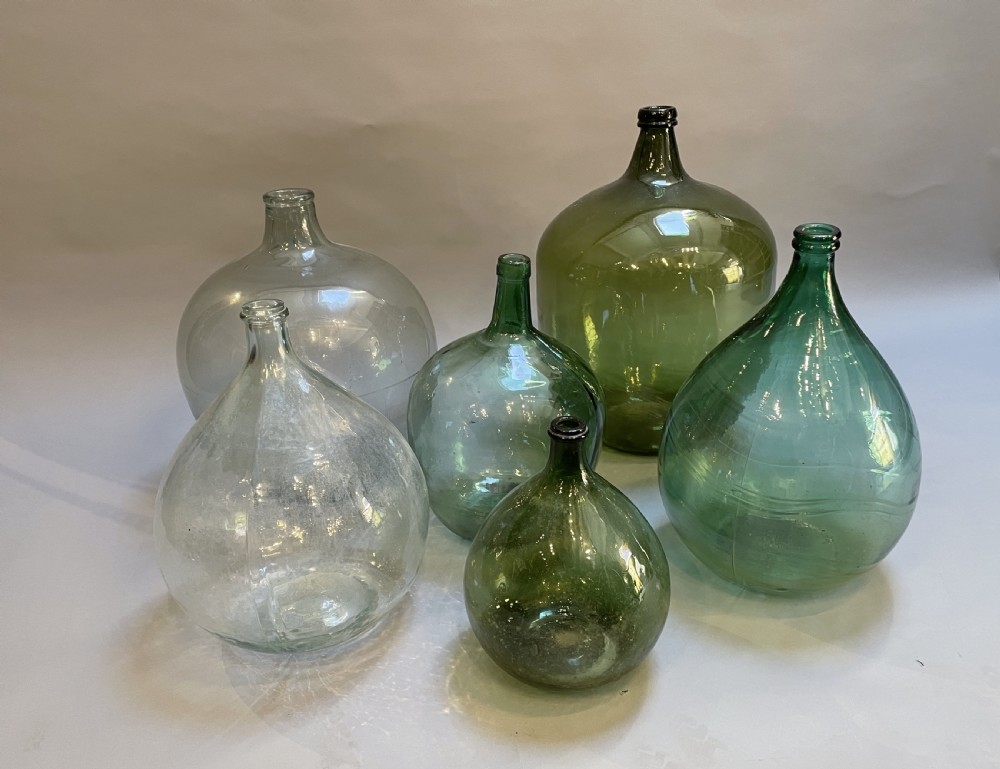 A collection of six antique French glass carboys and demijohns in varying sizes and shades of clear and green glass.