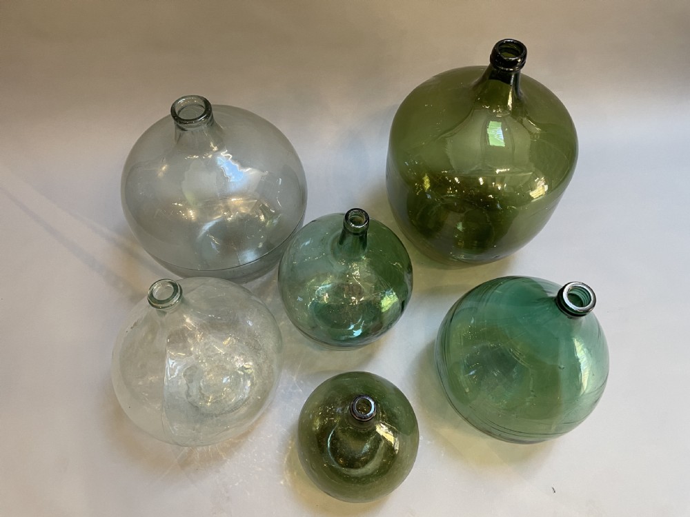 A collection of six antique French glass carboys and demijohns in varying sizes and shades of clear and green glass. View II
