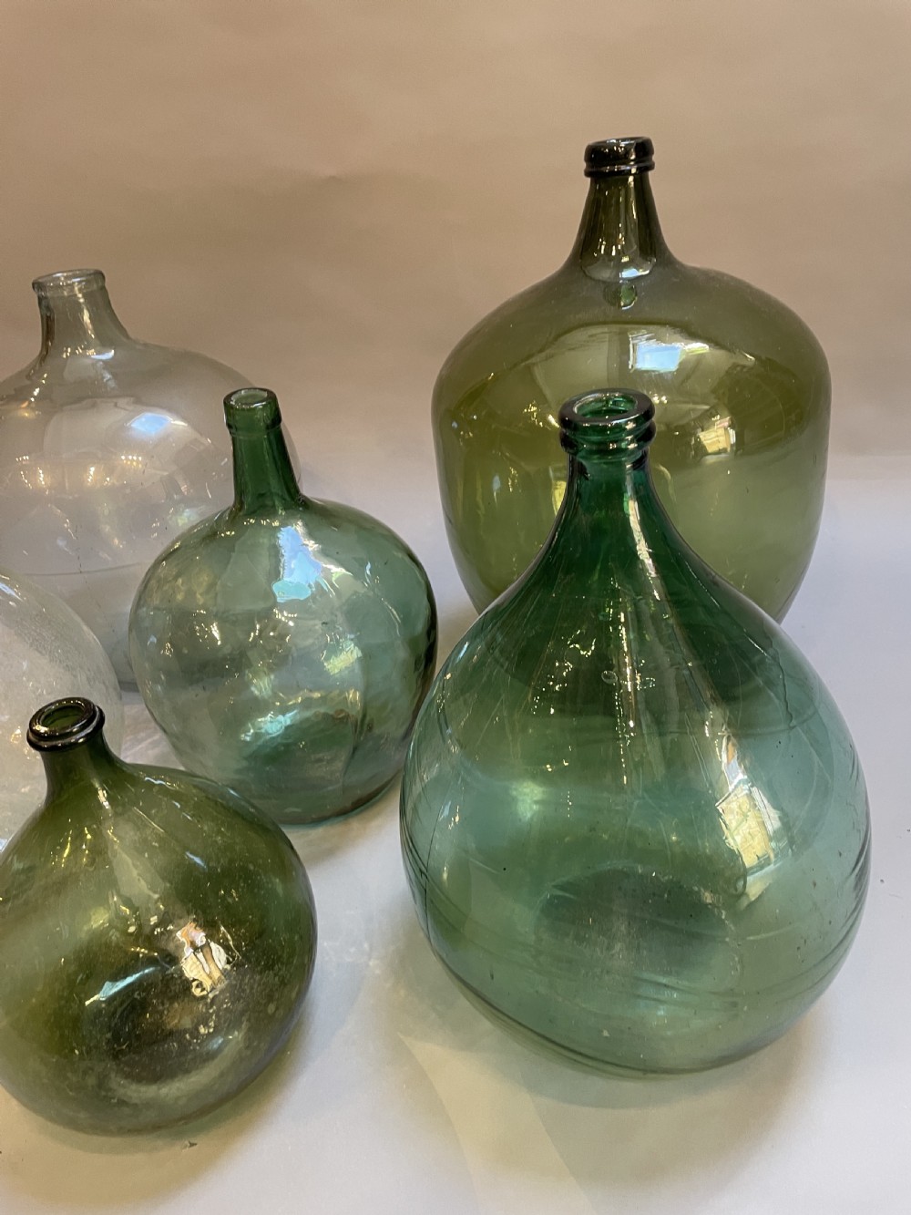 A collection of six antique French glass carboys and demijohns in varying sizes and shades of clear and green glass. View III