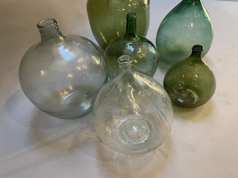A collection of six antique French glass carboys and demijohns in varying sizes and shades of clear and green glass. View IV