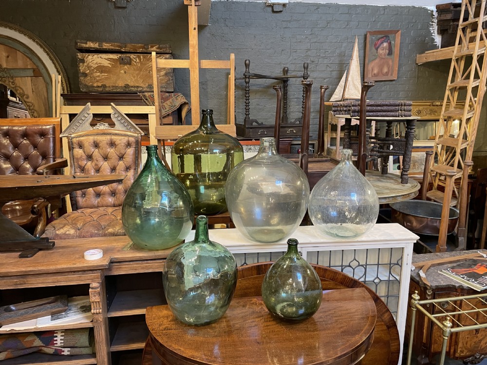 A collection of six antique French glass carboys and demijohns in varying sizes and shades of clear and green glass. View V