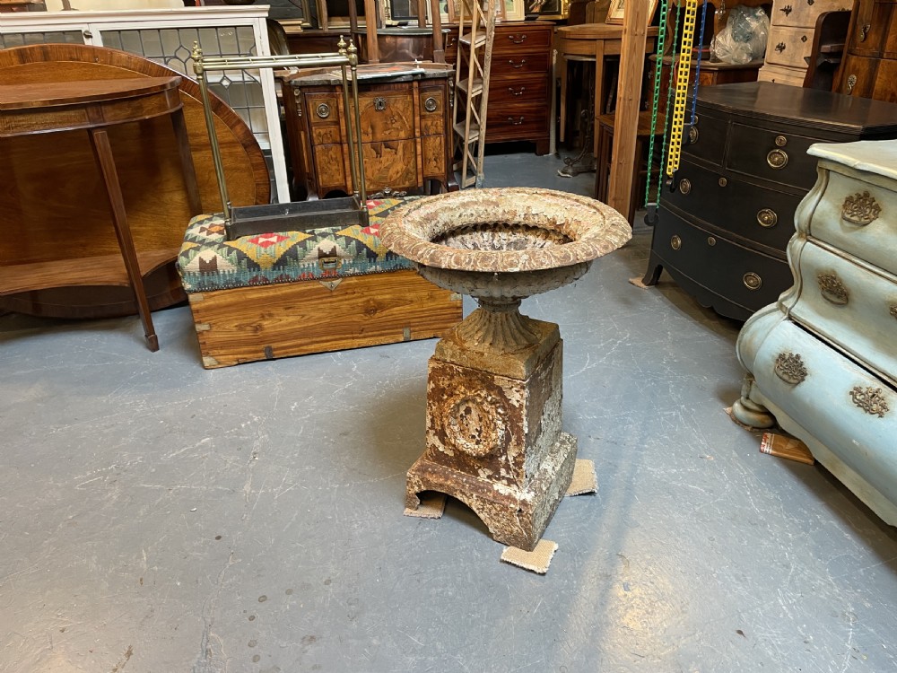 A Victorian cast iron garden urn with a fluted rim and laurel wreath medallion base, displaying a weathered white paint finish over oxidised iron. View V
