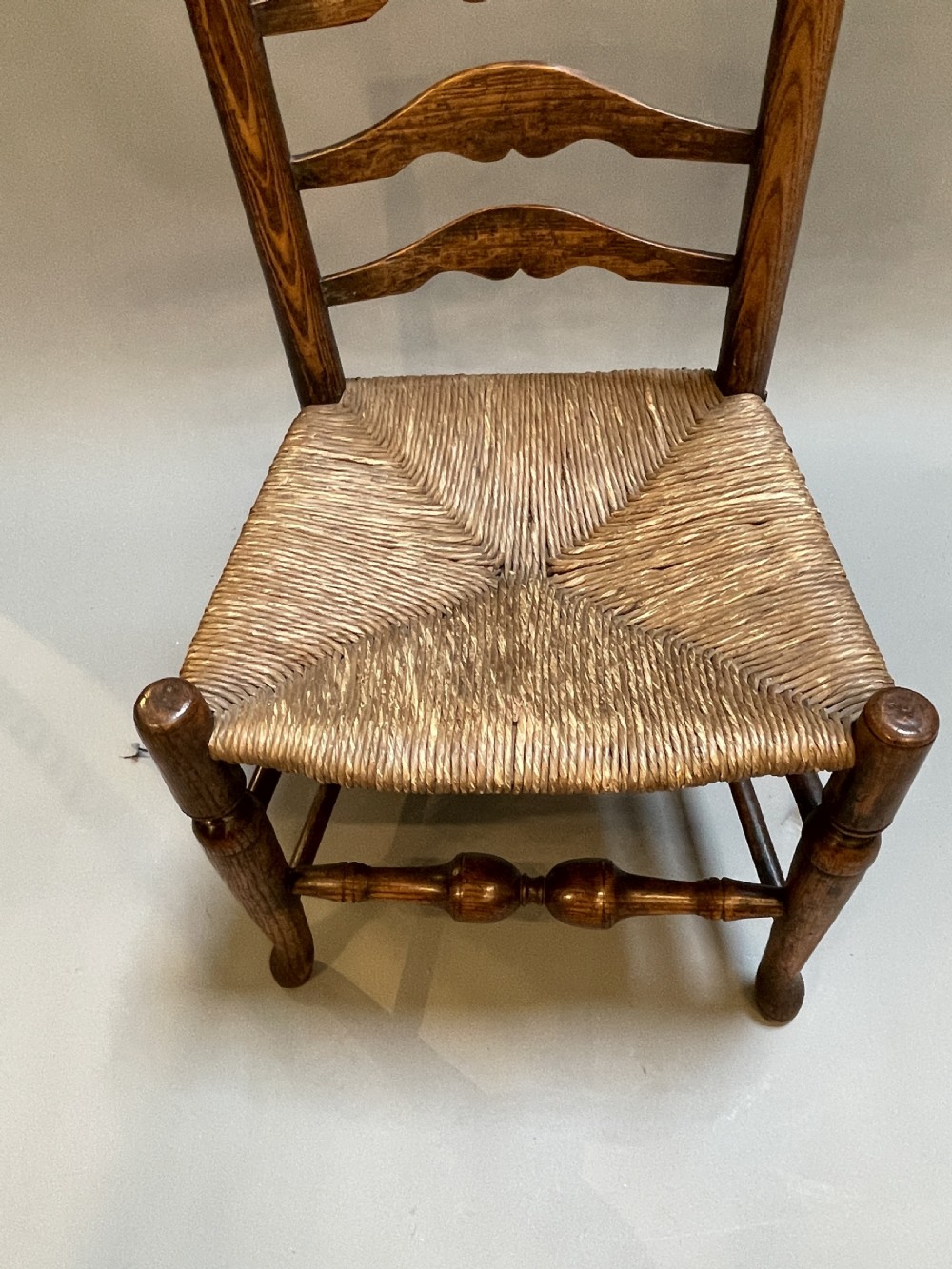 A wooden country side chair featuring a ladderback with four wavy horizontal slats, turned front legs, and a woven rush seat. View II