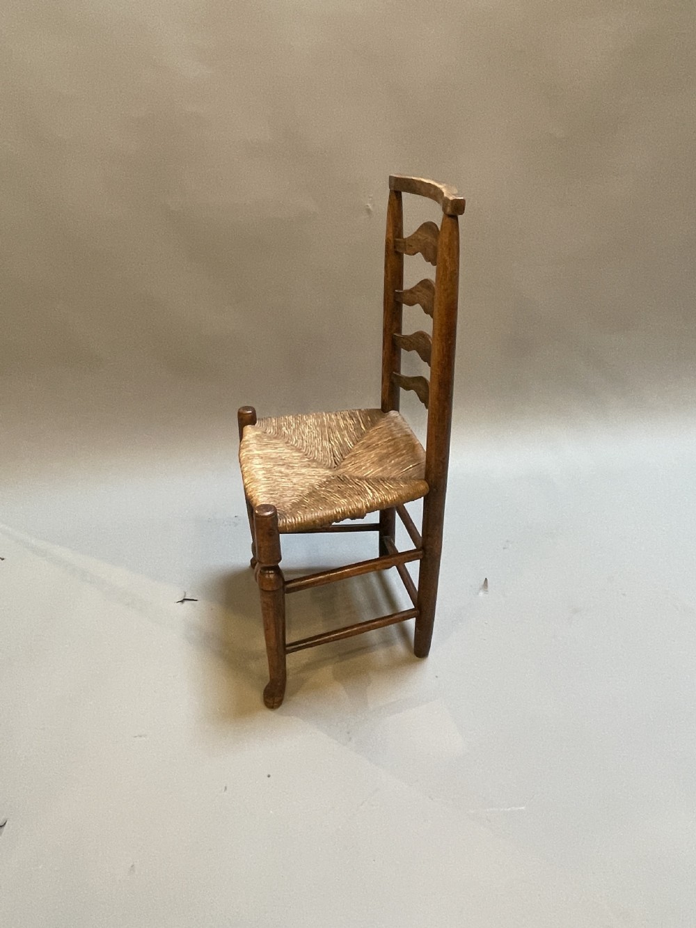 A wooden country side chair featuring a ladderback with four wavy horizontal slats, turned front legs, and a woven rush seat. View III