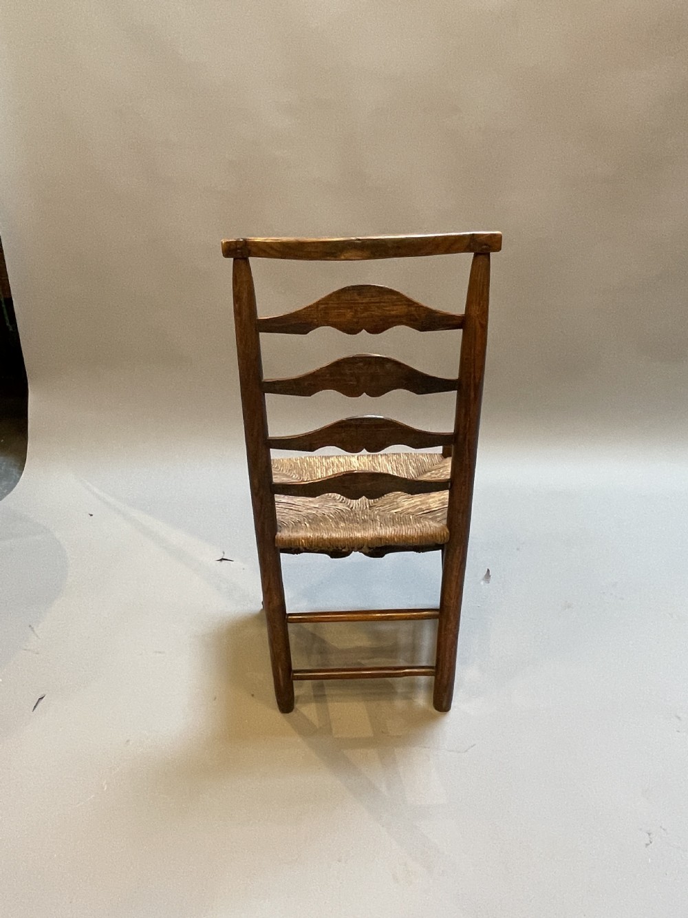 A wooden country side chair featuring a ladderback with four wavy horizontal slats, turned front legs, and a woven rush seat. View IV