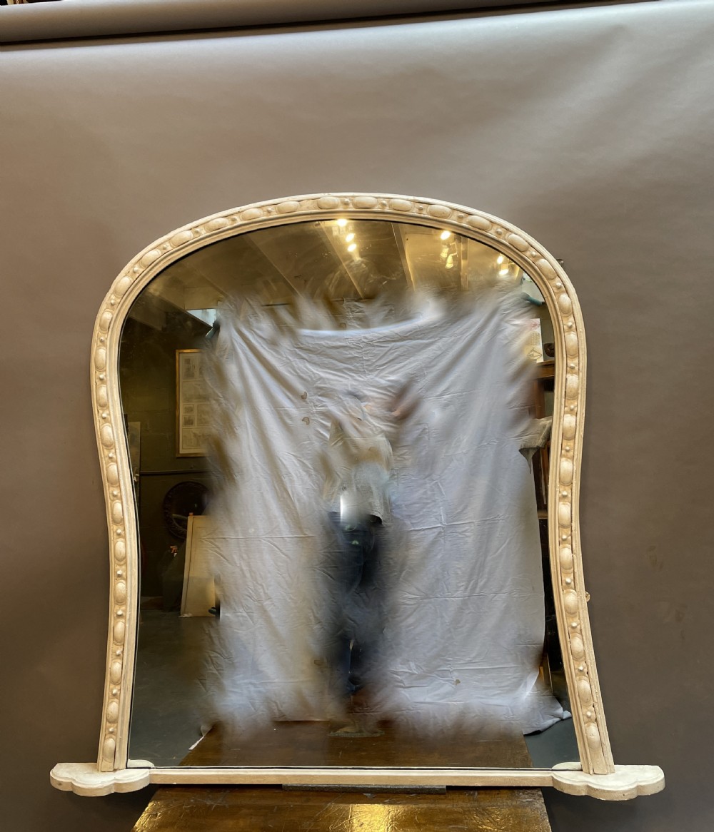 A 19th-century arched overmantel mirror featuring an off-white painted frame decorated with beaded moulding and small projecting feet.