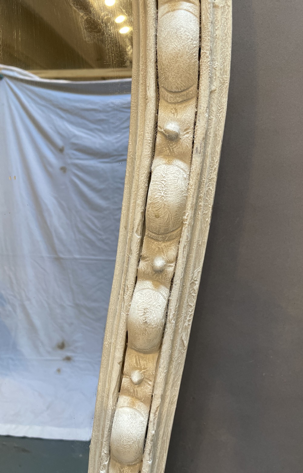 A 19th-century arched overmantel mirror featuring an off-white painted frame decorated with beaded moulding and small projecting feet. View II