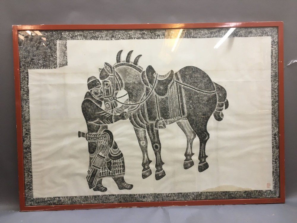 A large monochrome framed paper rubbing depicting a groom attending to a saddled Tang Dynasty horse.