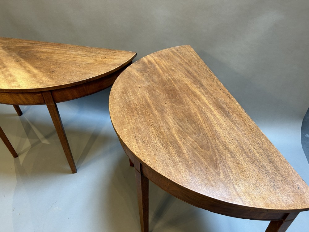 A pair of George III mahogany semi-circular demilune console tables supported by square tapered legs. View II