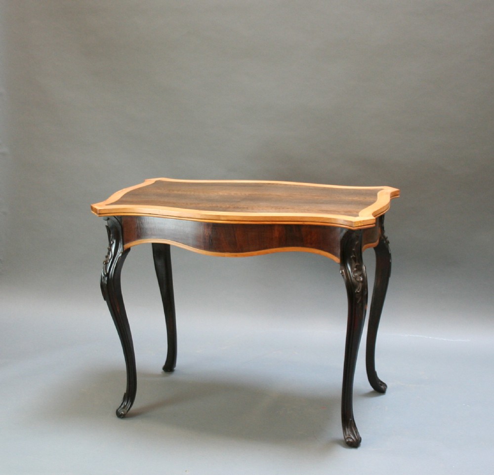 A 19th-century Ceylonese serpentine centre table featuring dark hardwood construction, a light wood crossbanded top, and carved cabriole legs.