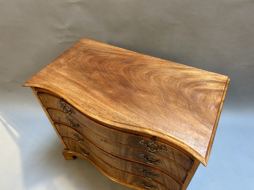 A 19th-century mahogany chest of drawers featuring a serpentine front, four graduated drawers with ornamental brass handles, and bracket feet. View II