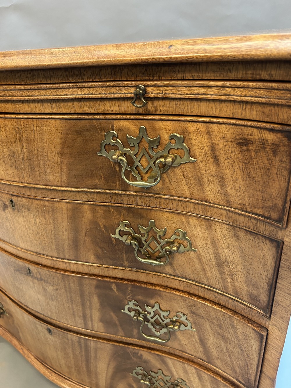 A 19th-century mahogany chest of drawers featuring a serpentine front, four graduated drawers with ornamental brass handles, and bracket feet. View V