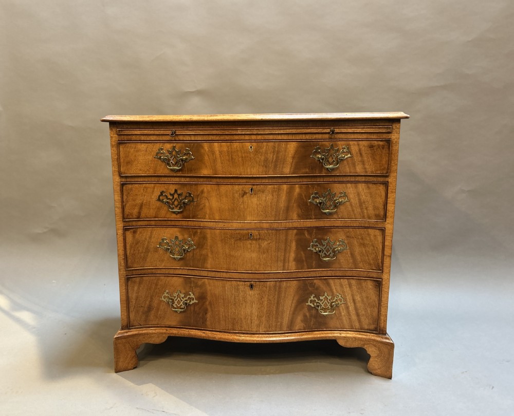 A 19th-century mahogany chest of drawers featuring a serpentine front, four graduated drawers with ornamental brass handles, and bracket feet. View VI