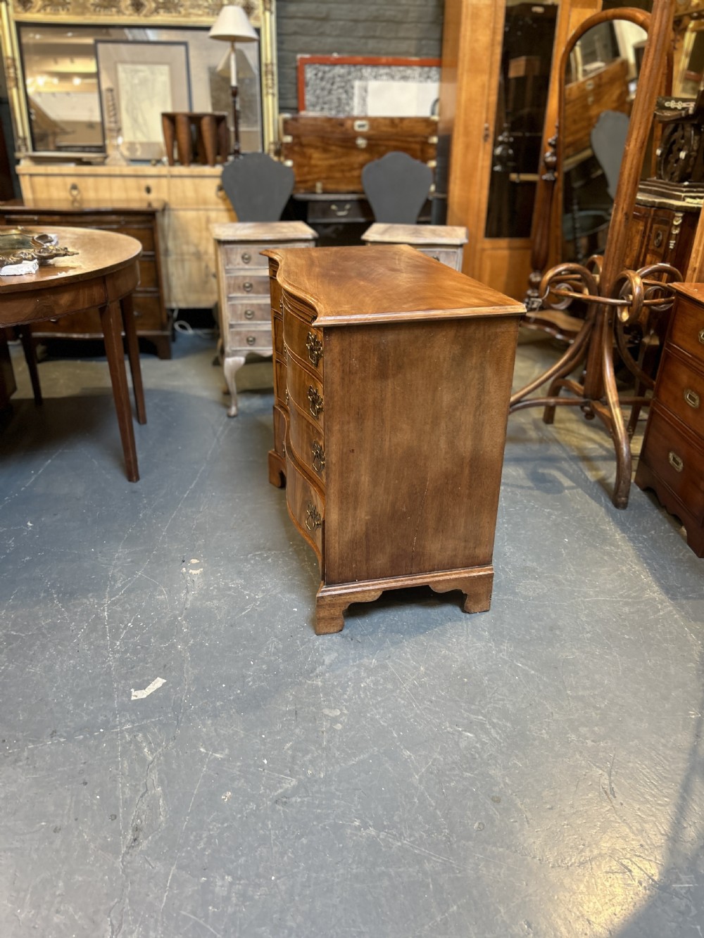 A 19th-century mahogany chest of drawers featuring a serpentine front, four graduated drawers with ornamental brass handles, and bracket feet. View IX