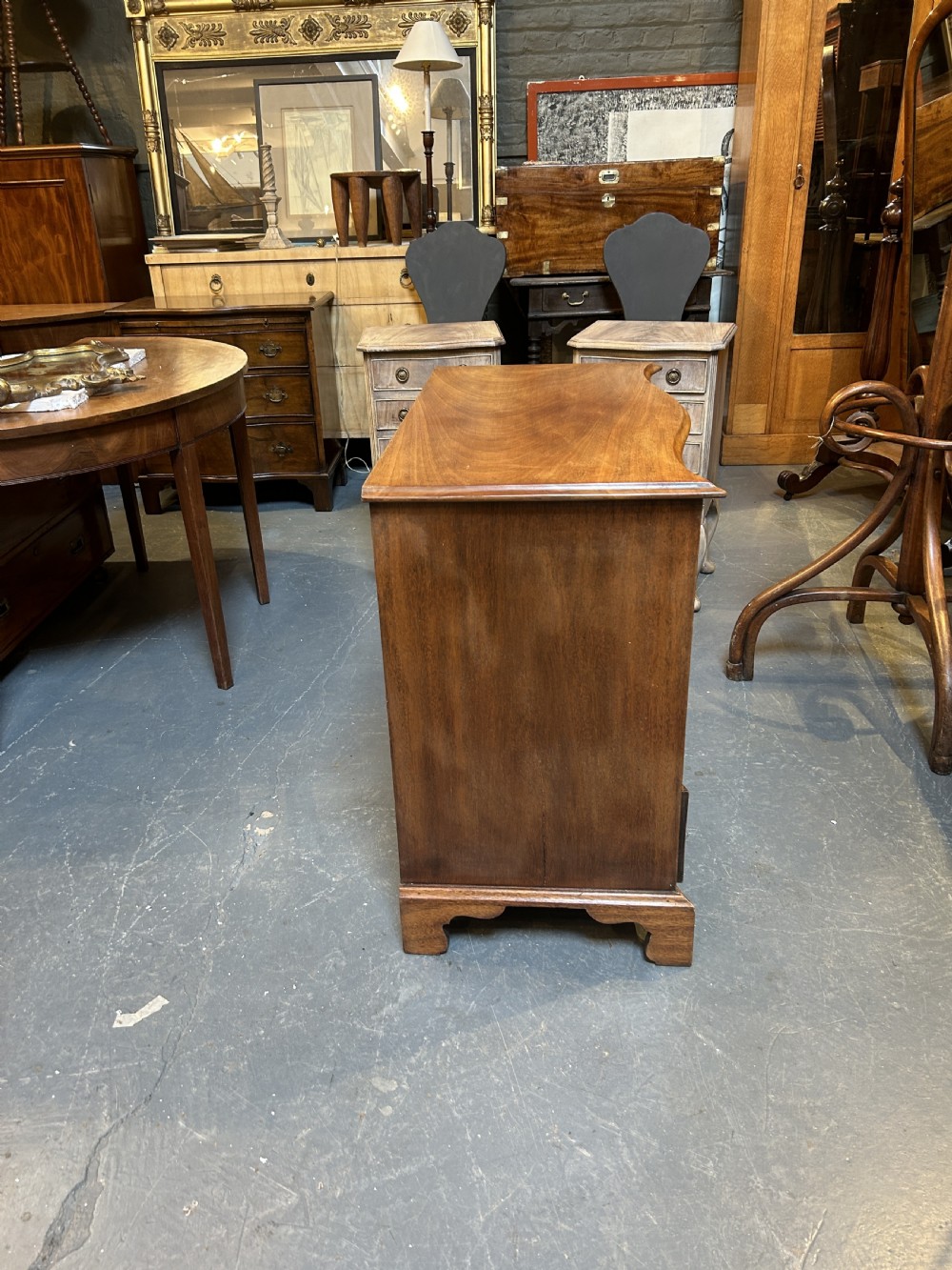 A 19th-century mahogany chest of drawers featuring a serpentine front, four graduated drawers with ornamental brass handles, and bracket feet. View XI