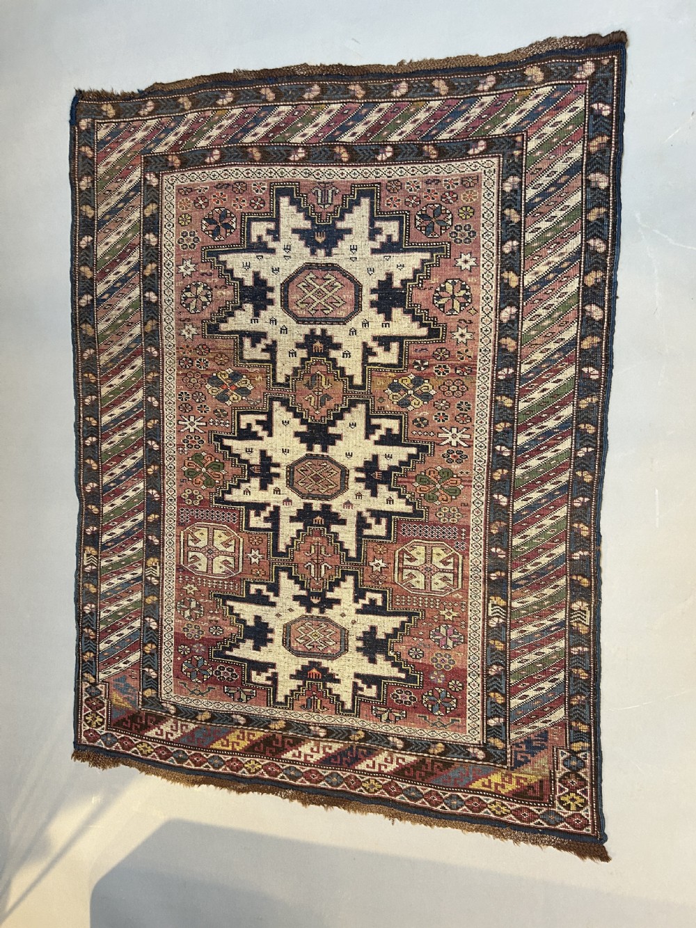An antique Caucasian Kazak wool rug featuring three cream latch-hook medallions on a terracotta red field with geometric borders.