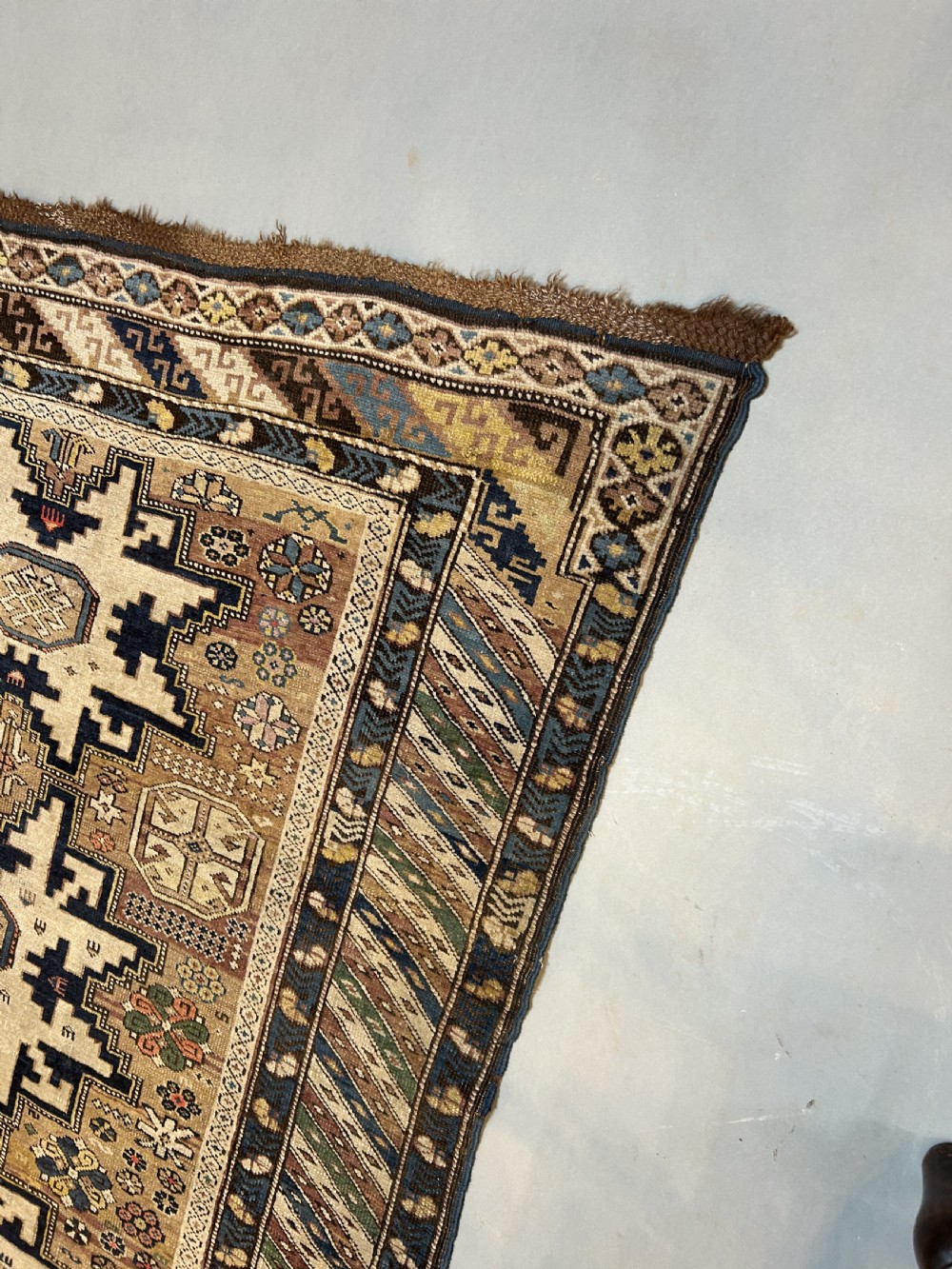 An antique Caucasian Kazak wool rug featuring three cream latch-hook medallions on a terracotta red field with geometric borders. View III