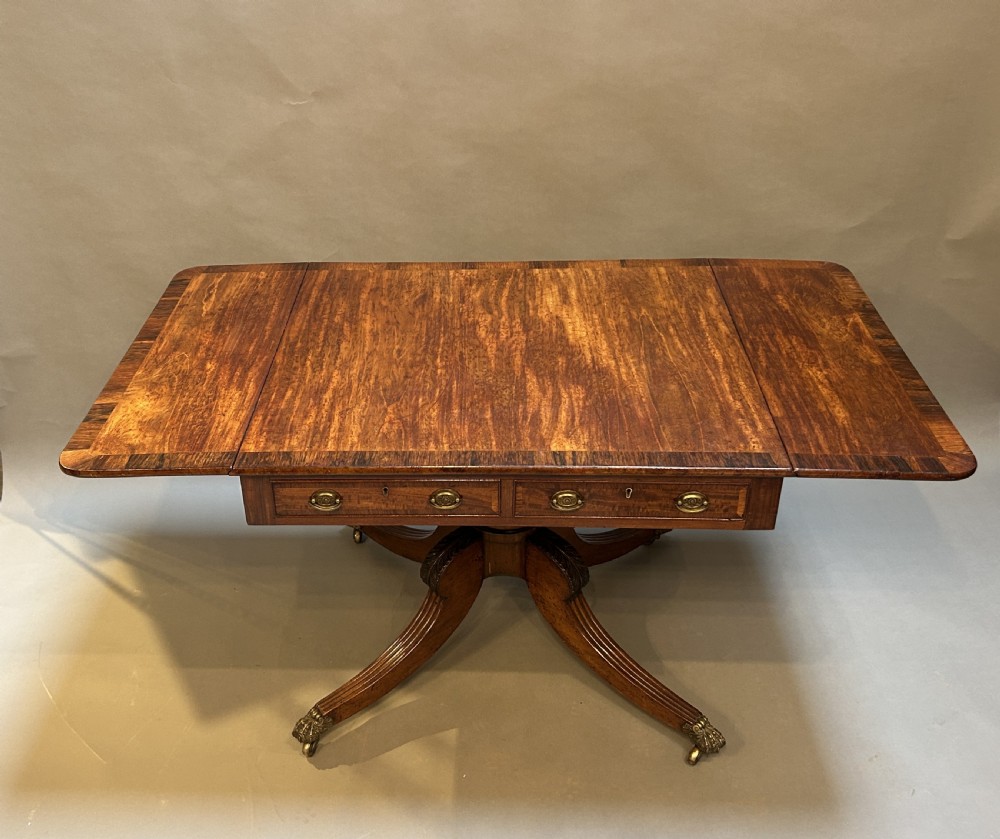 A George IV mahogany sofa table featuring drop leaves, frieze drawers with brass handles, and a reeded quadruped pedestal base with brass castors. View III