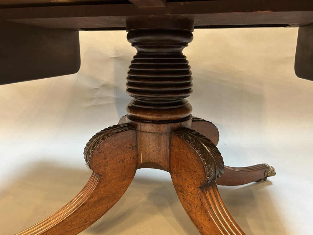 A George IV mahogany sofa table featuring drop leaves, frieze drawers with brass handles, and a reeded quadruped pedestal base with brass castors. View V