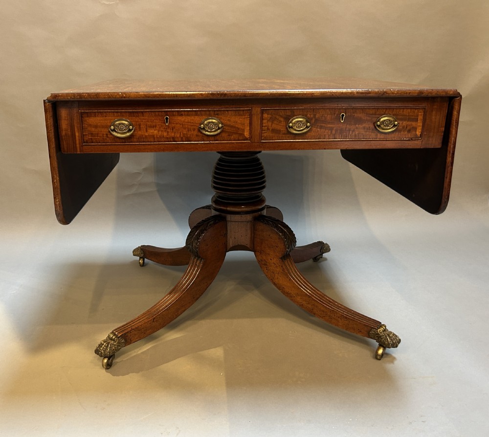 A George IV mahogany sofa table featuring drop leaves, frieze drawers with brass handles, and a reeded quadruped pedestal base with brass castors. View VIII