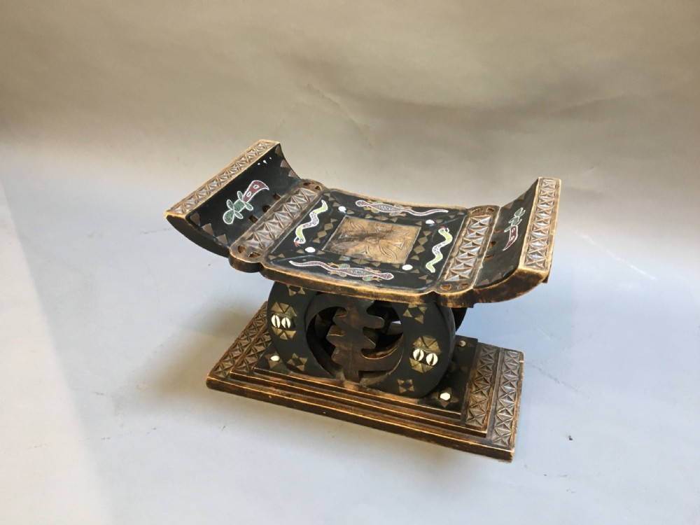 A hand-carved dark timber Ashanti stool featuring a curved seat with inlaid motifs, a central openwork column, and a rectangular carved base.